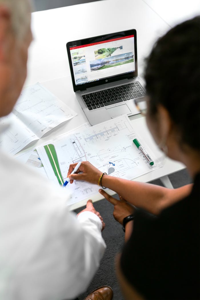 services-03 Engineers collaborate on designs with blueprints and laptops in a modern office setting.